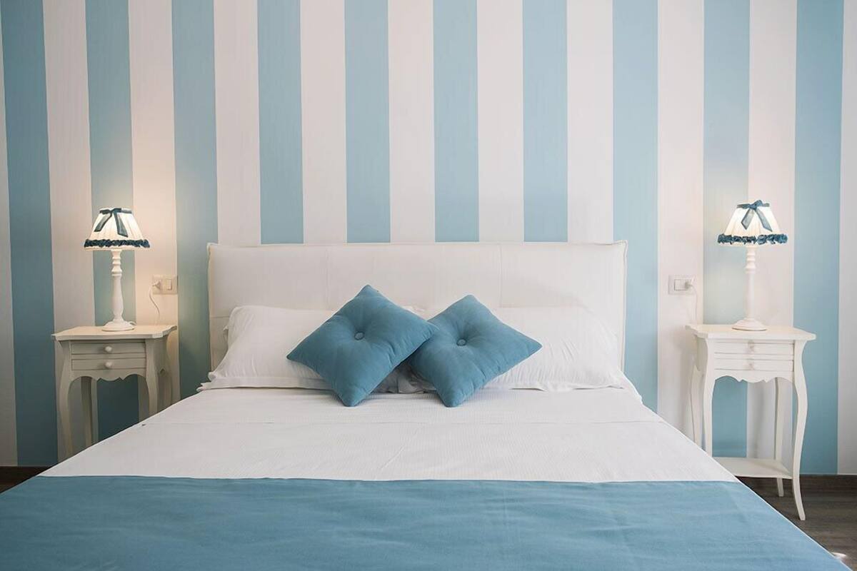A bed with white bedding and two blue pillows, flanked by two bedside tables with lamps.