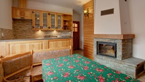 A kitchen with wooden cabinets, a stone fireplace, and a table with a floral tablecloth. - Apartament Krupowki 73 - 7 Person (Zakopane)