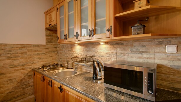 A kitchen with granite countertops, stainless steel appliances, wooden cabinets with glass doors, and a stone backsplash. - Apartament Krupowki 73 - 7 Person (Zakopane)