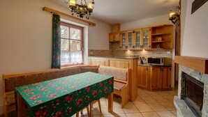 A kitchen with wooden cabinets, a dining table with floral tablecloth, and a fireplace. - Apartament Krupowki 73 - 7 Person (Zakopane)