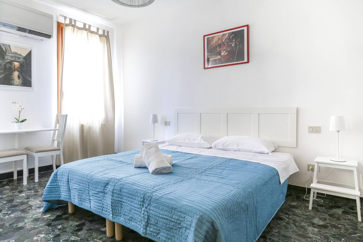 A hotel room with a bed, a desk, a chair, and a window with curtains.