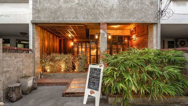L’entrée d’un restaurant avec un menu écrit à la craie, un intérieur en bois et une grande plante en bambou à l’extérieur.