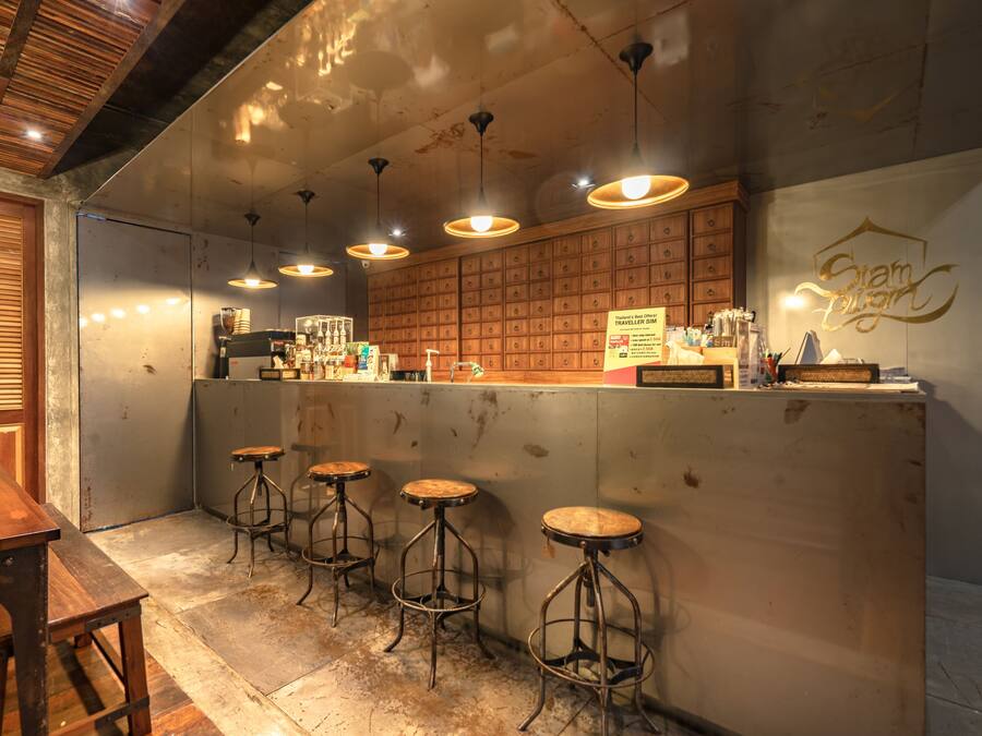 Zona de bar con taburetes de madera, mostrador y cartel que dice 'Siam Light'.