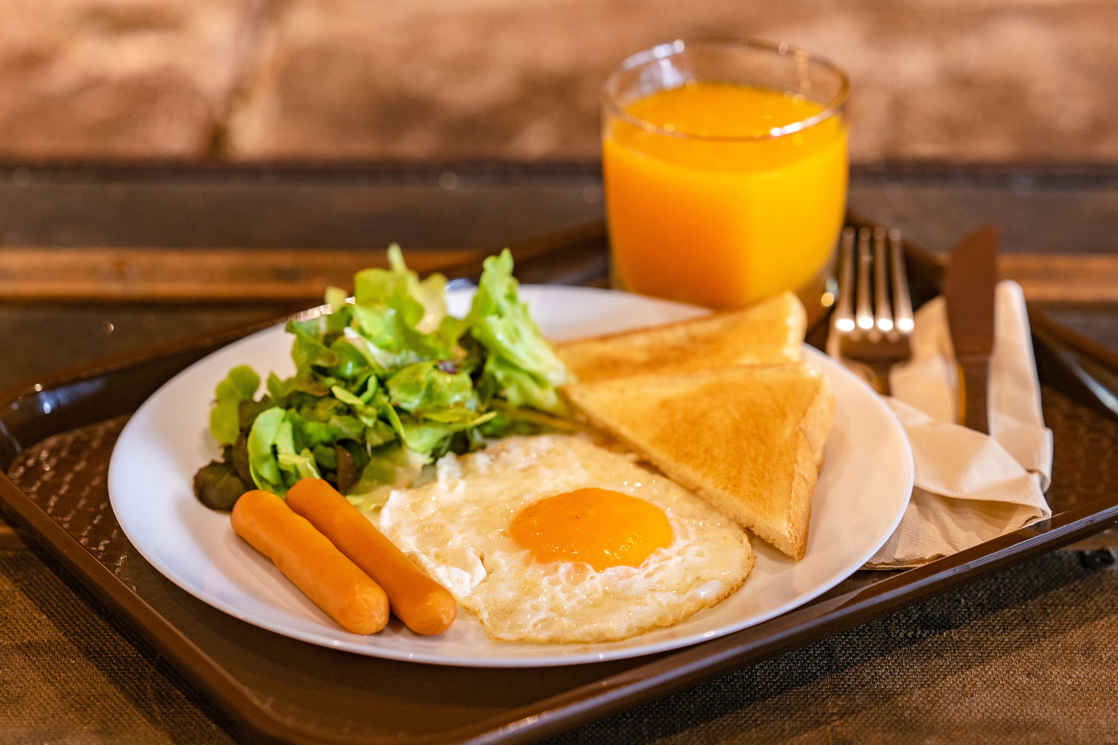 A breakfast plate with toast, a fried egg, carrots, and a side salad, accompanied by a glass of orange juice.