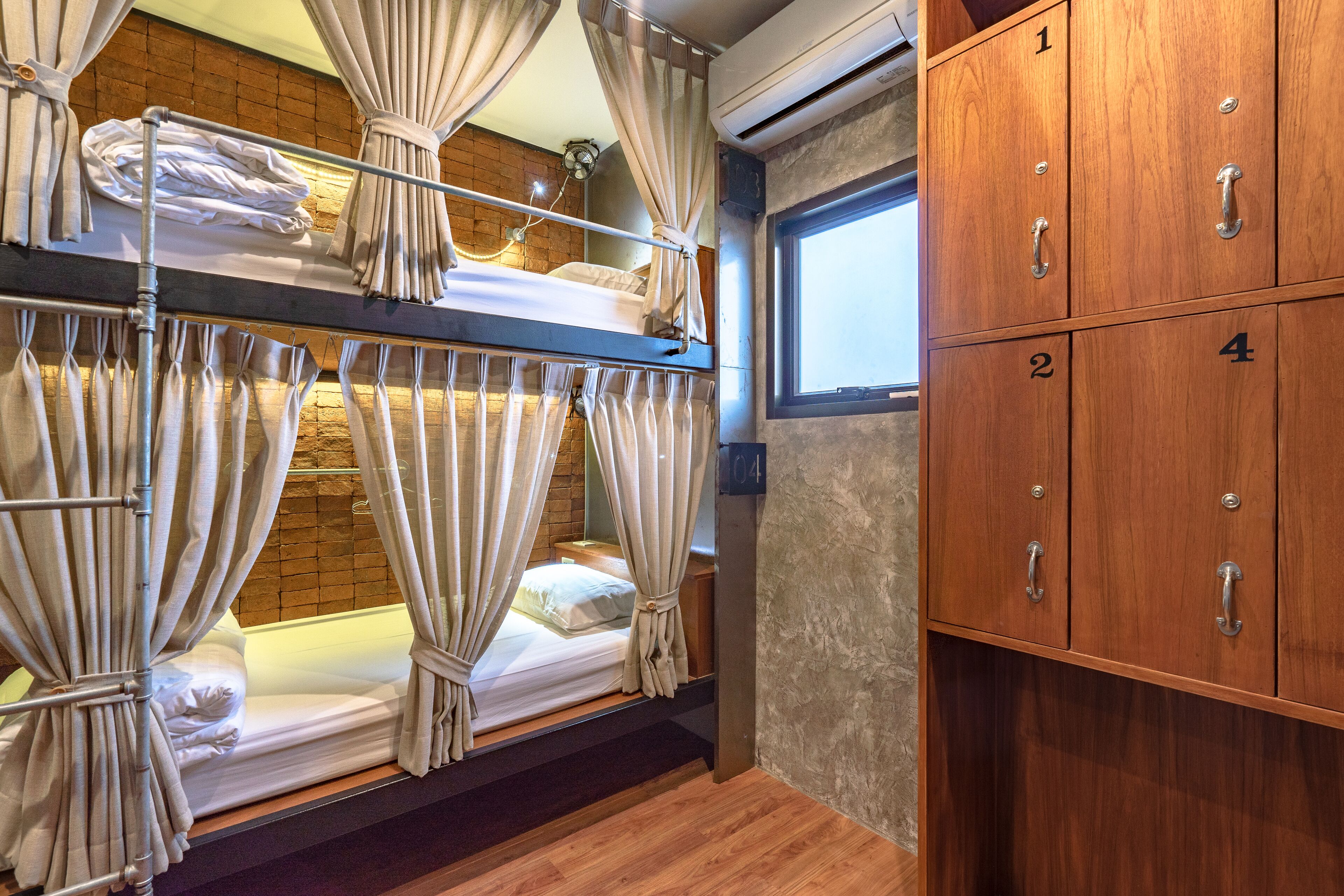 Un lit superposé avec des rideaux, une armoire en bois dotée de compartiments numérotés et un mur en briques.
