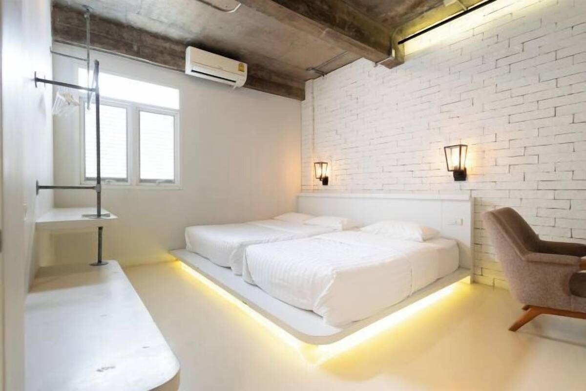 A modern hotel room with two beds, a white brick wall, and a window.