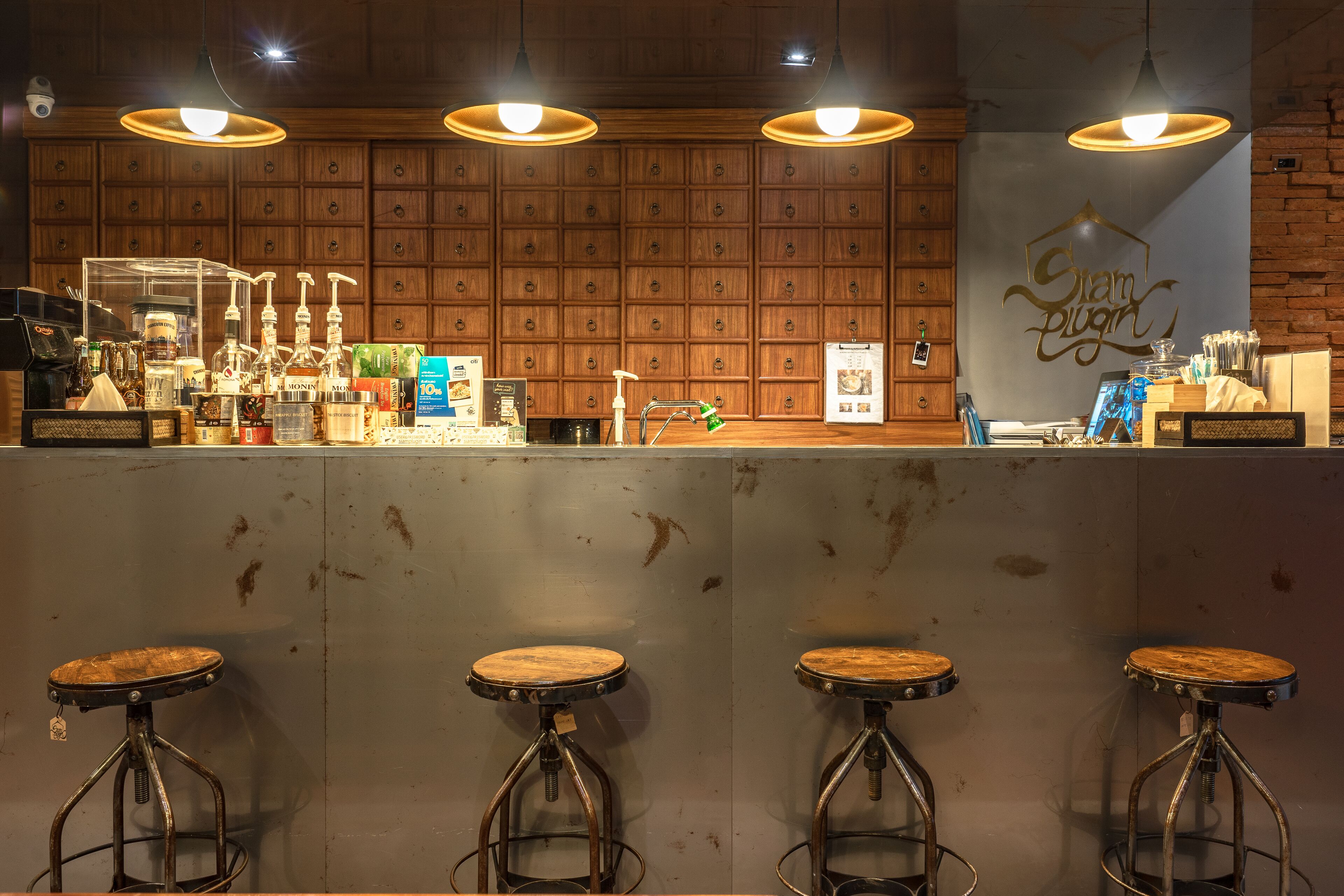 Un coin bar avec des lambris en bois, un comptoir où sont exposées différentes bouteilles et une enseigne indiquant « Slam Plug ». Il y a trois tabourets devant le bar.