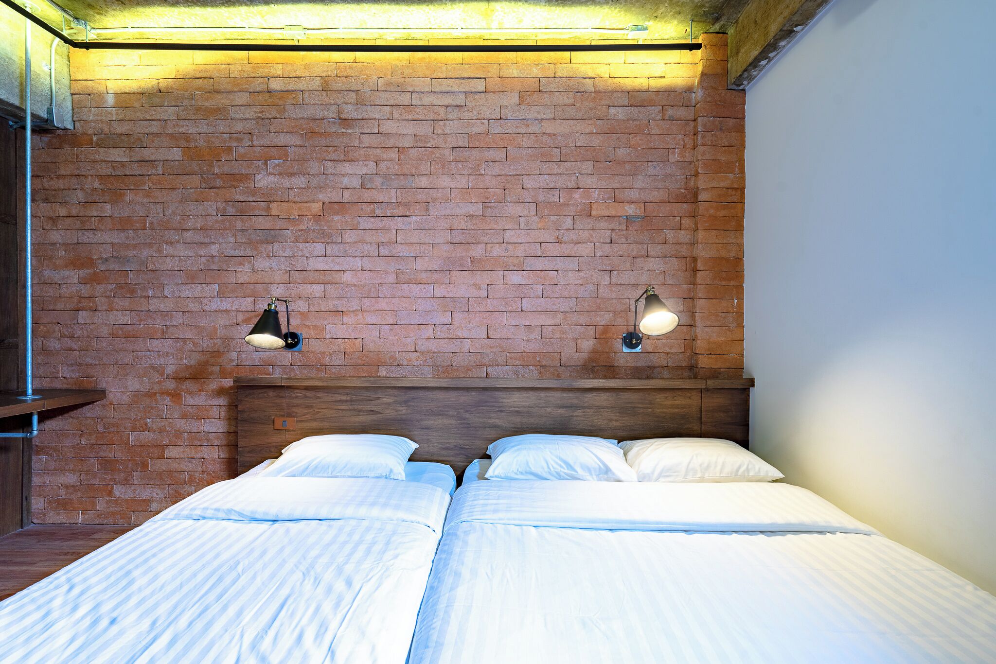 Un lit double avec du linge de lit blanc, un mur en briques et deux lampes fixées au mur.