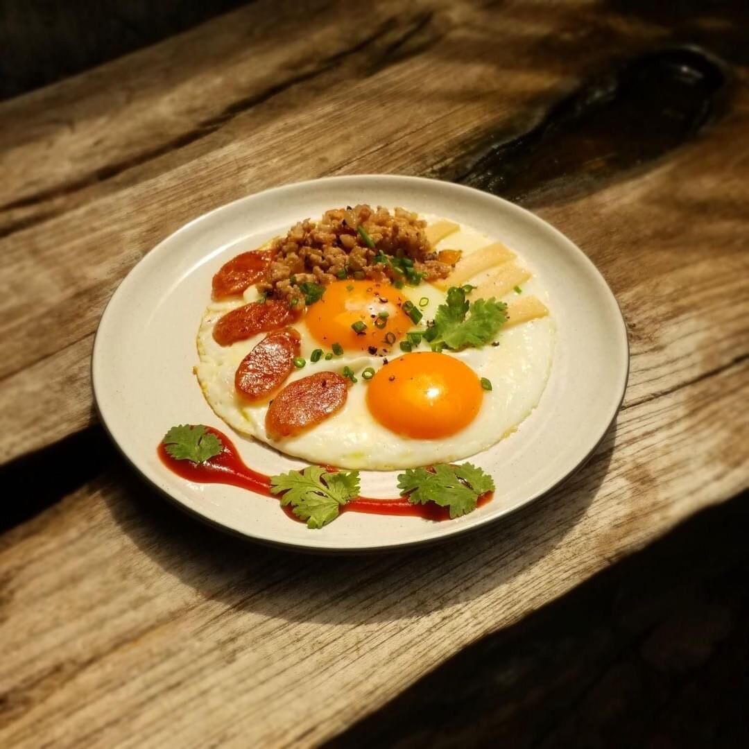 Prato de comida com ovos, salsicha e molho sobre uma mesa de madeira.