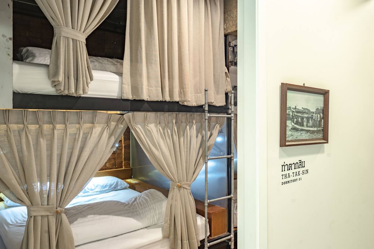 A dormitory room with bunk beds, curtains, a framed picture on the wall, and a wooden headboard.