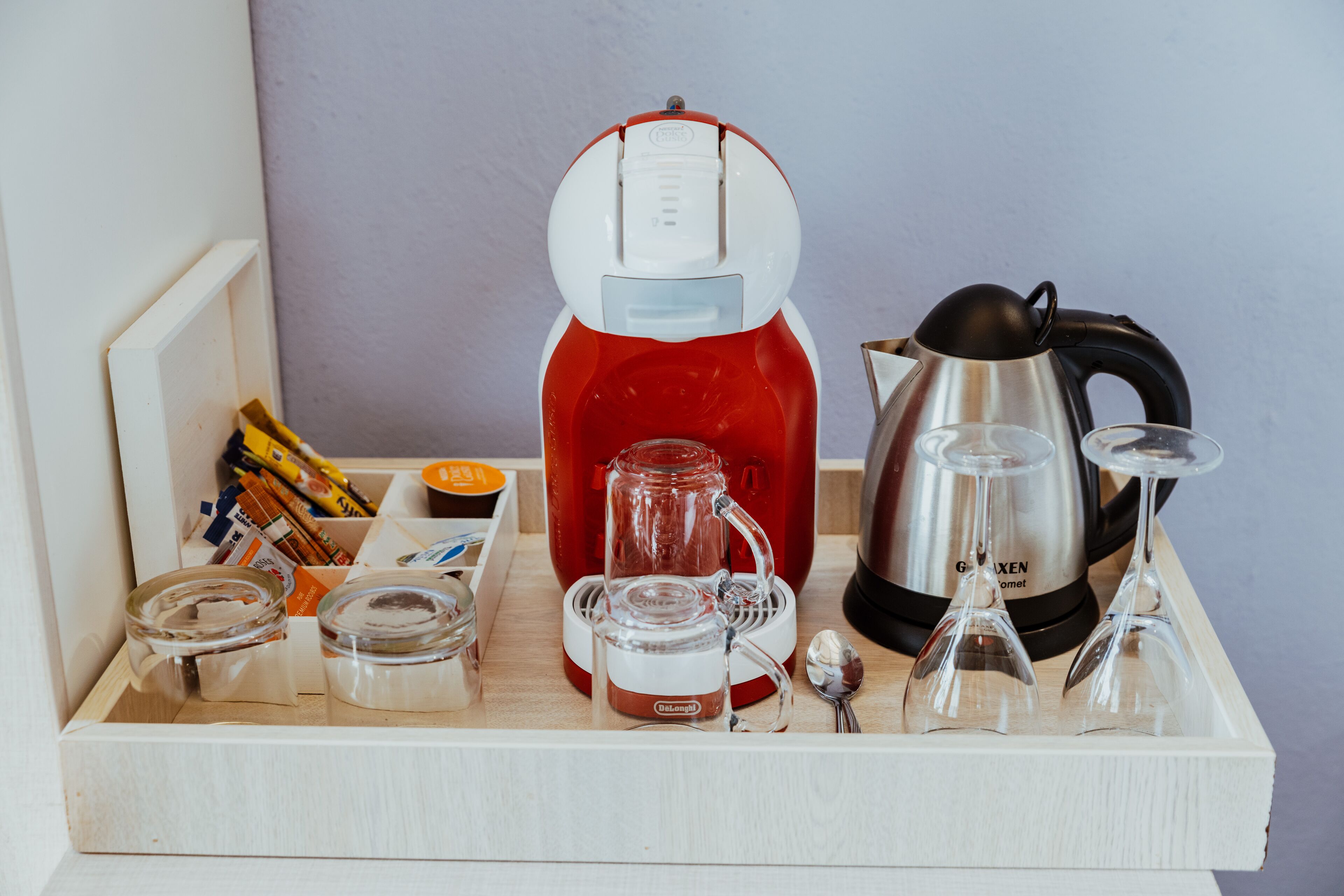 A tray with a red coffee maker, a silver electric kettle, and two wine glasses.