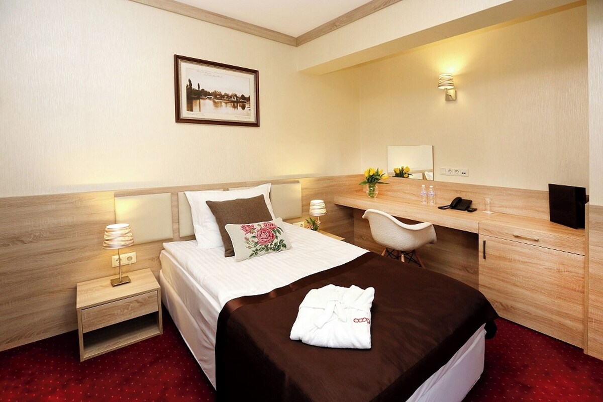 Una habitación de hotel con cama, mesita de noche, lámpara, silla, escritorio y espejo.