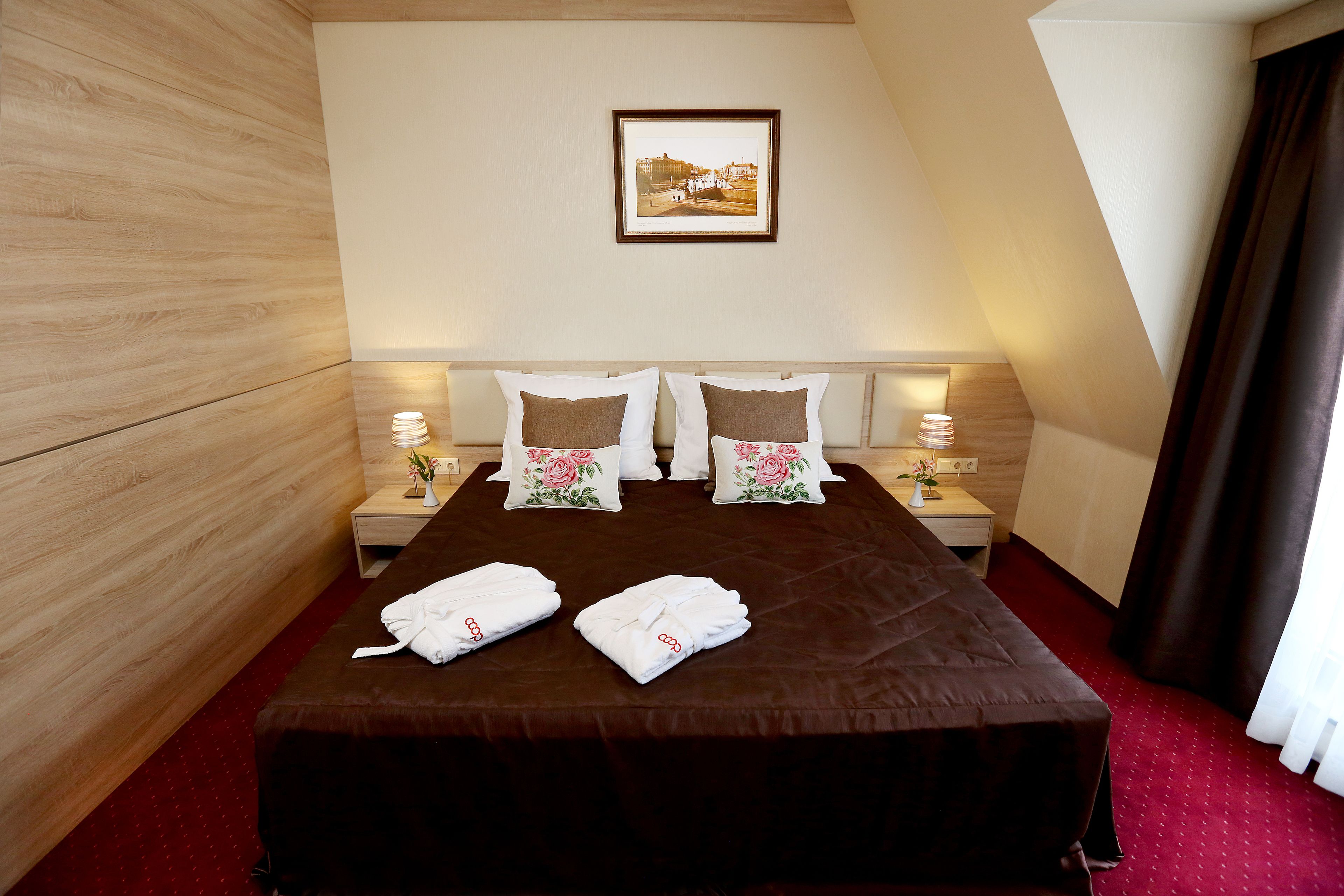 Habitación de hotel con una cama grande, dos mesitas de noche, un cuadro enmarcado en la pared y una alfombra roja.