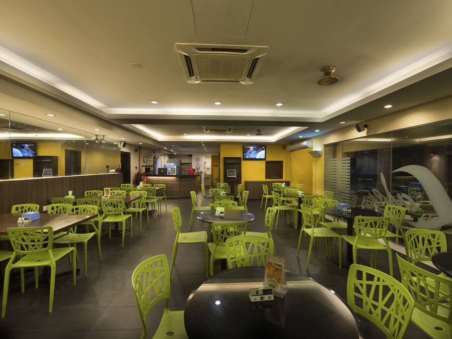 A restaurant with green chairs and tables, a counter, and a television on the wall.