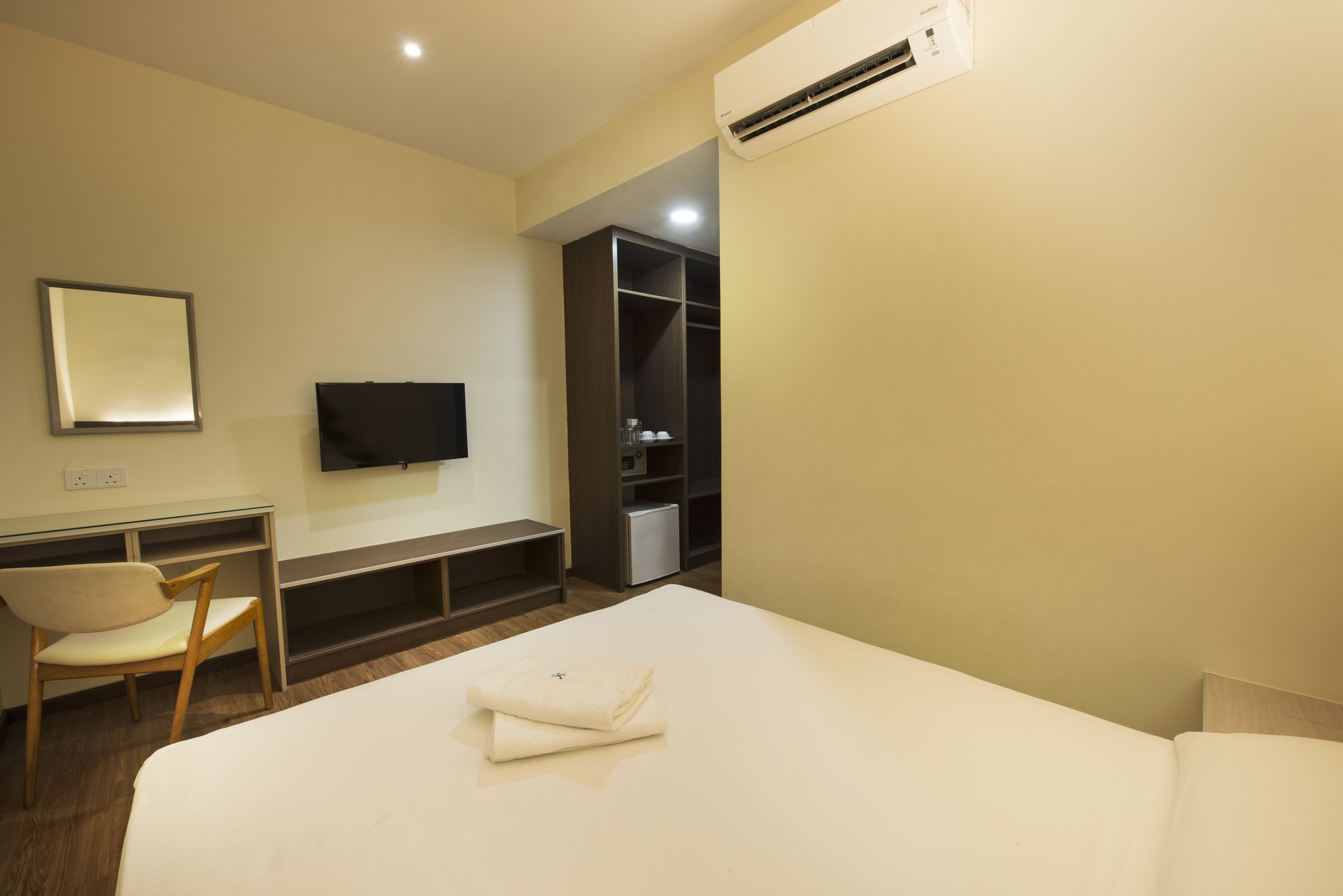 A hotel room with a bed, a desk with a chair, a television, and a wardrobe.
