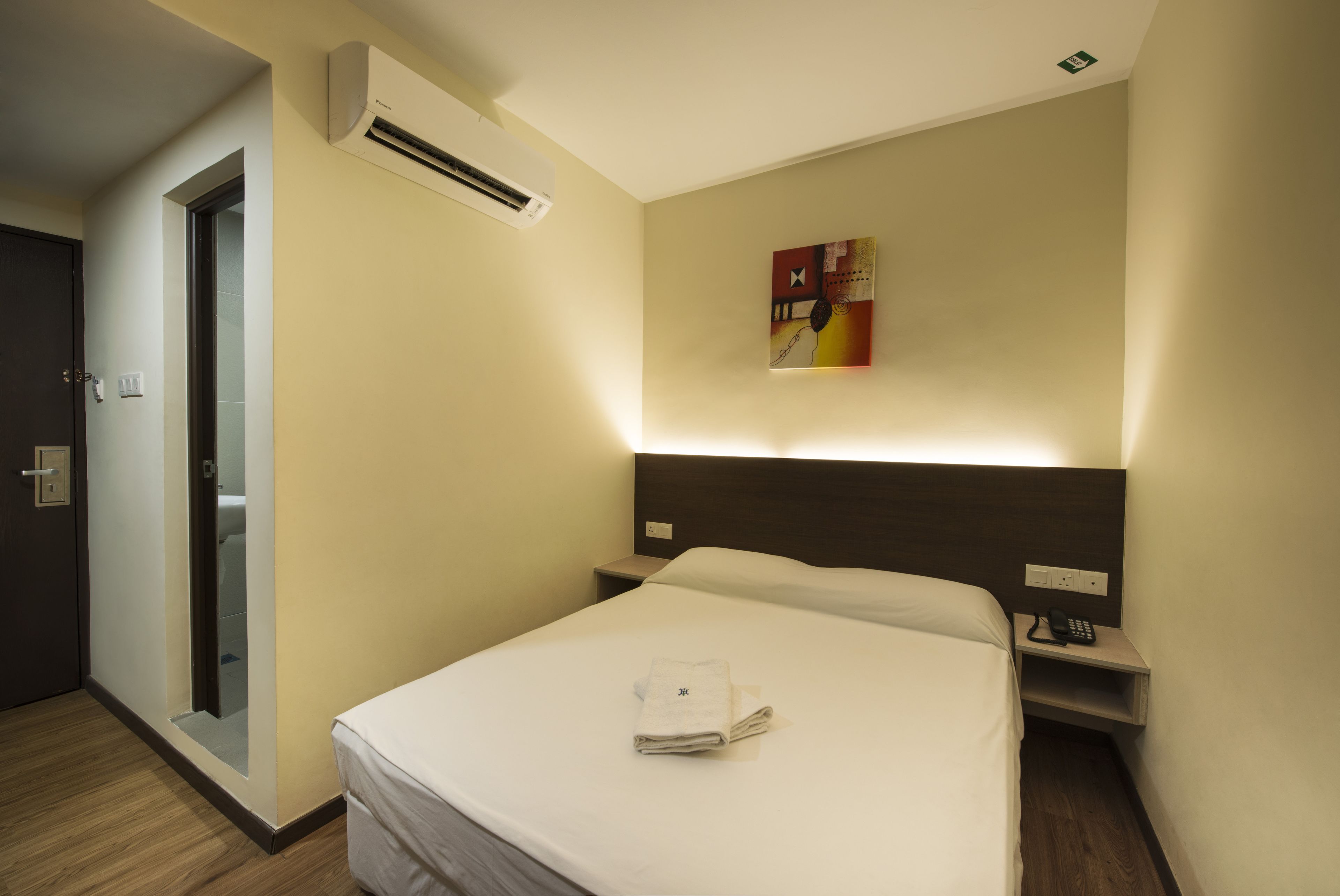 A hotel room with a bed, bedside table, and an air conditioning unit.