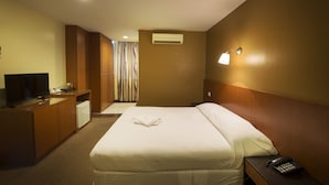 Hotelkamer met een bed, een bureau met een televisie, een minibar, een wandairconditioner en een telefoon naast het bed.