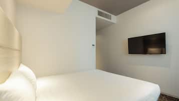 A hotel room with a bed, a chair, a TV mounted on the wall, and a visible air vent.
