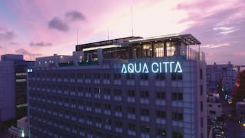 Um hotel chamado AQUA CITTA, com design arquitetônico moderno, apresentando um terraço no terraço e um grande letreiro iluminado.