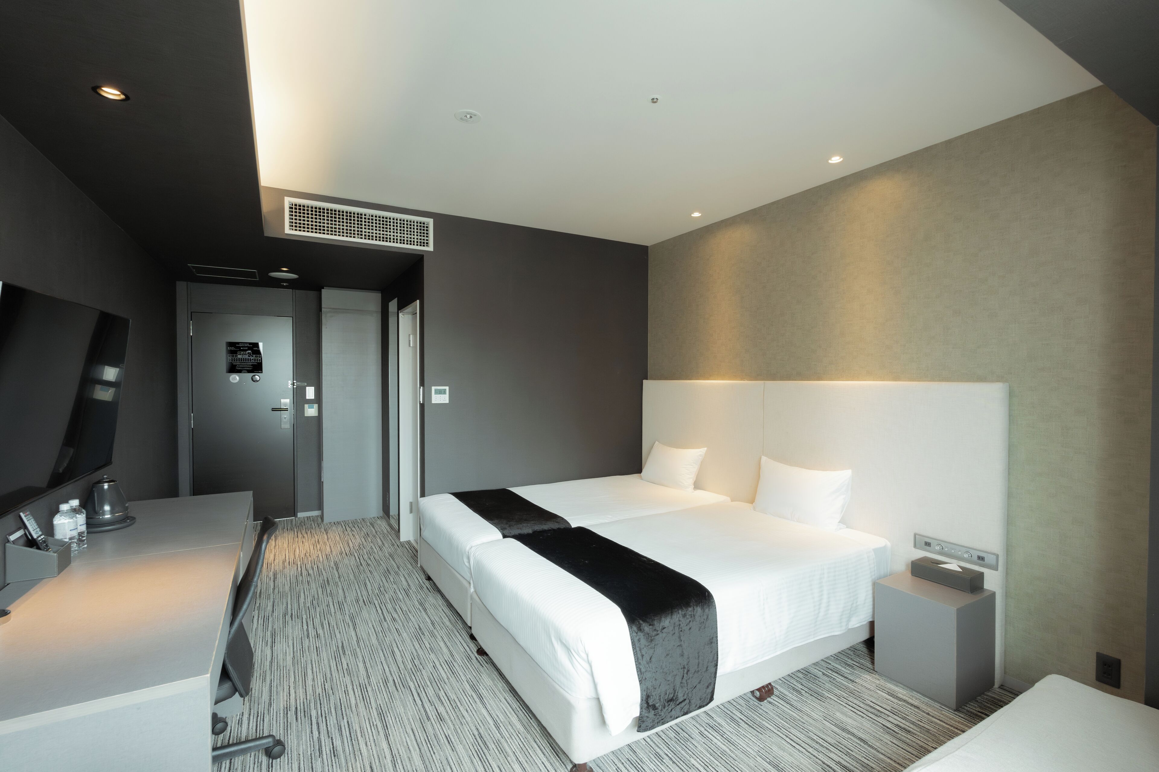 A modern hotel room with a large bed, bedside tables, a flat-screen TV, and a desk with a chair.