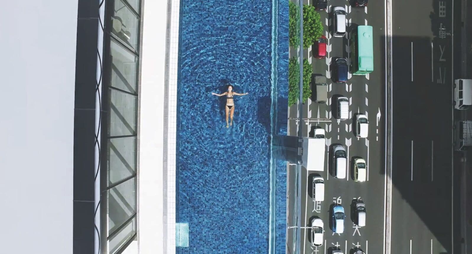A person in a swimming pool with a view of parked cars and a building.