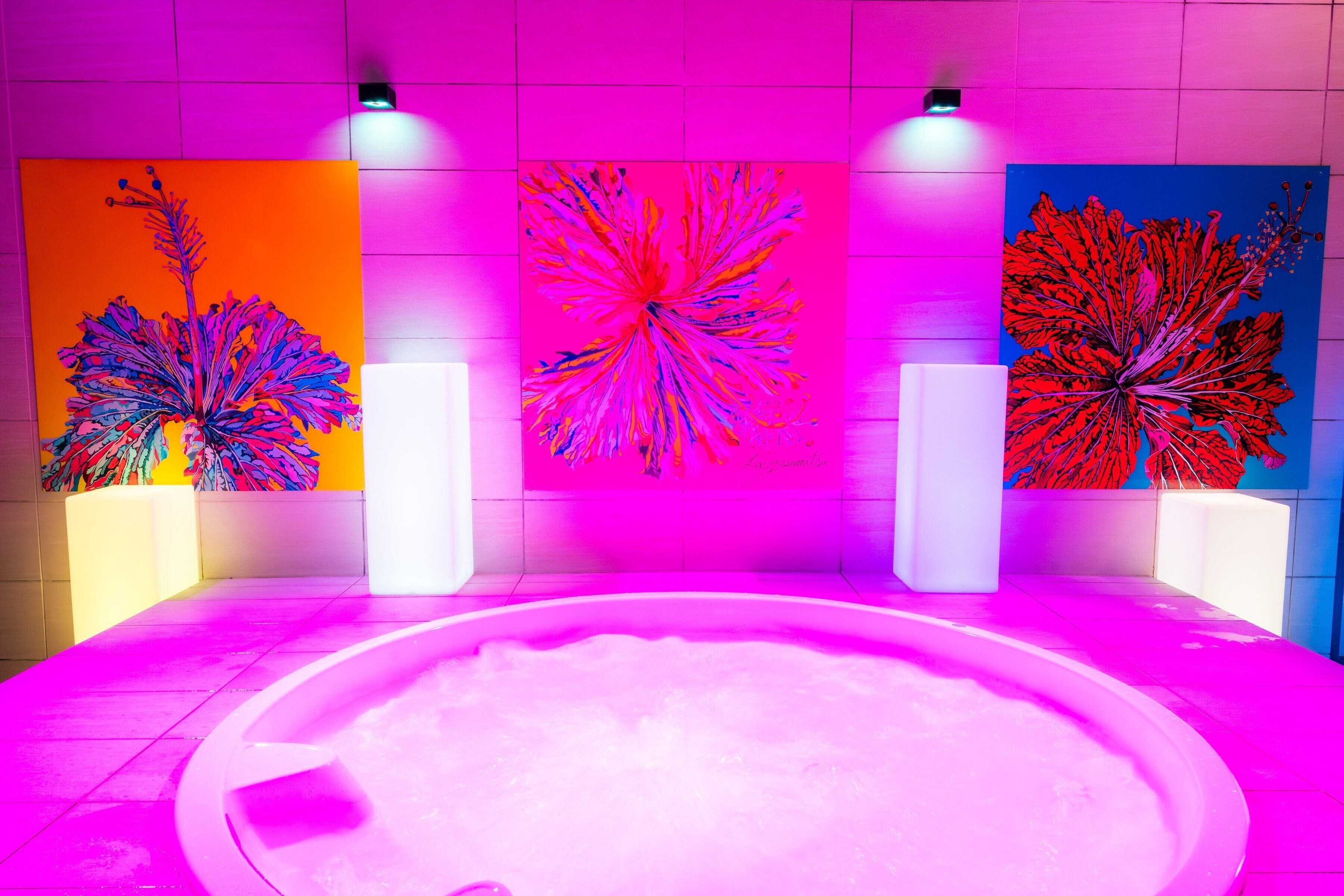 Un moderno espacio de spa con un jacuzzi central, rodeado de llamativas obras de arte abstracto en la pared.