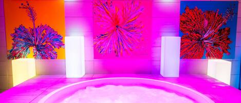 Un moderno espacio de spa con un jacuzzi central, rodeado de llamativas obras de arte abstracto en la pared.