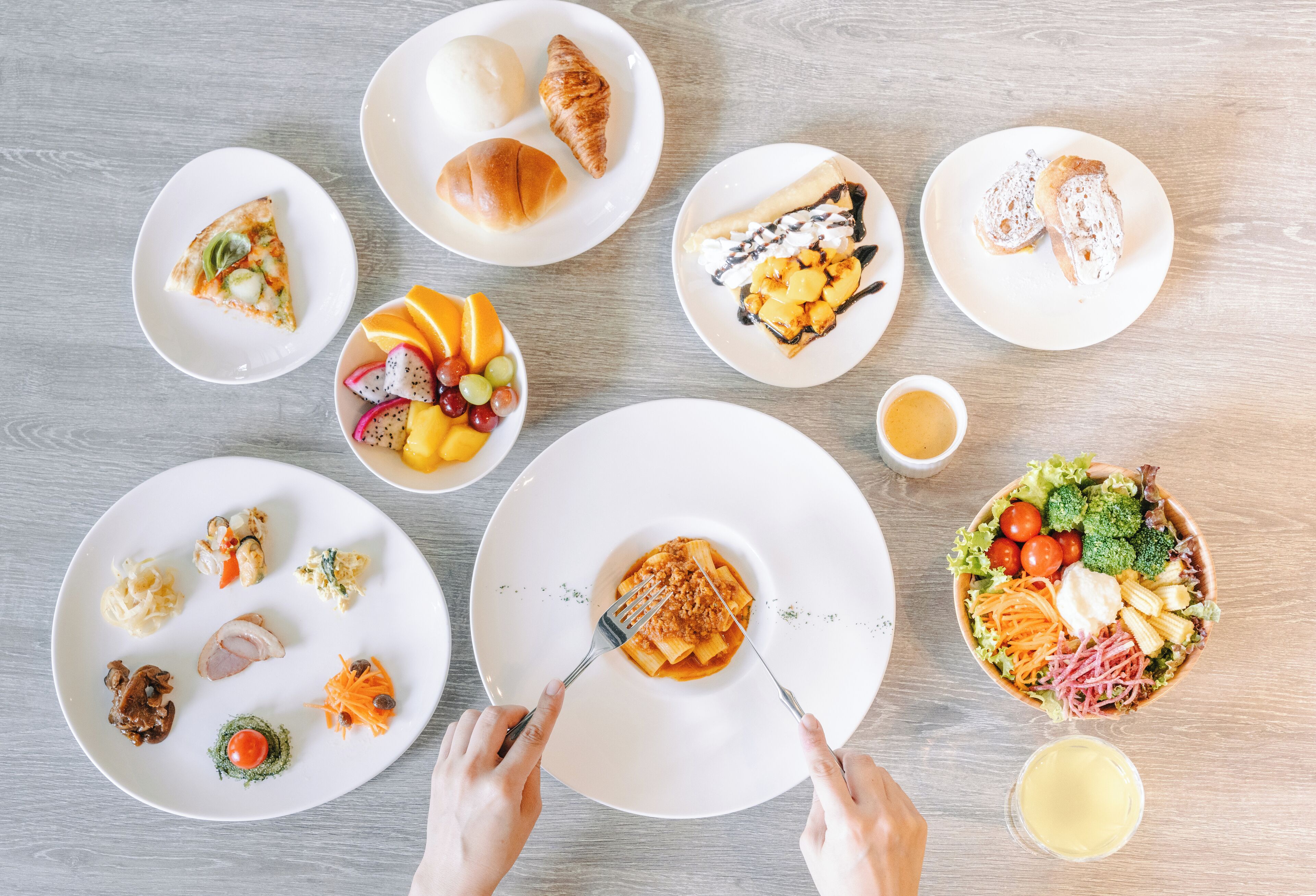A variety of dishes on plates, including pizza, pasta, and salads, arranged on a wooden table.