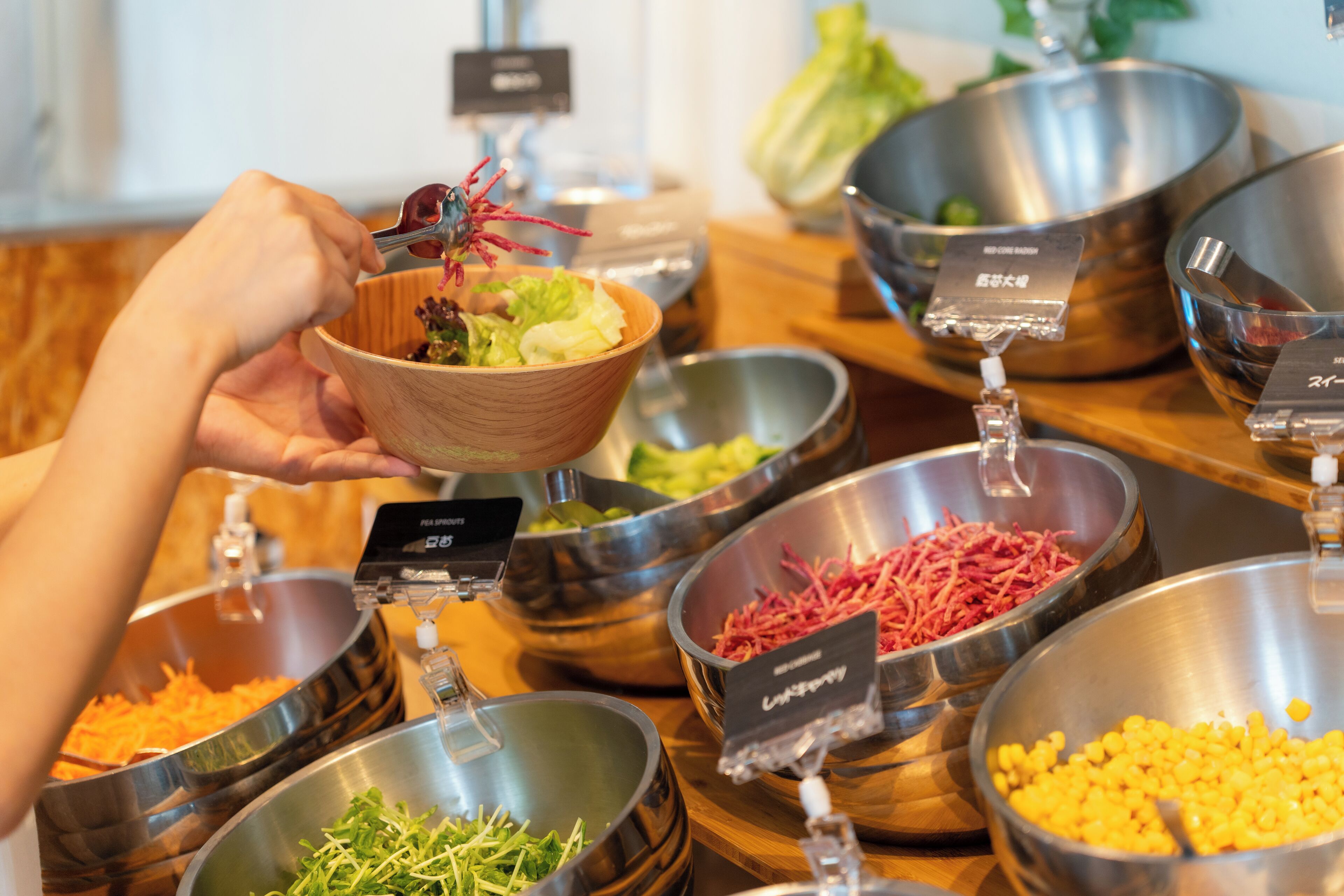 A buffet with various food items in metal bowls, including shredded cheese, corn, and leafy greens.