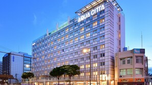 Un hotel moderno con un llamativo letrero Aqua Citta, que presenta una fachada en forma de cuadrícula y múltiples ventanales.