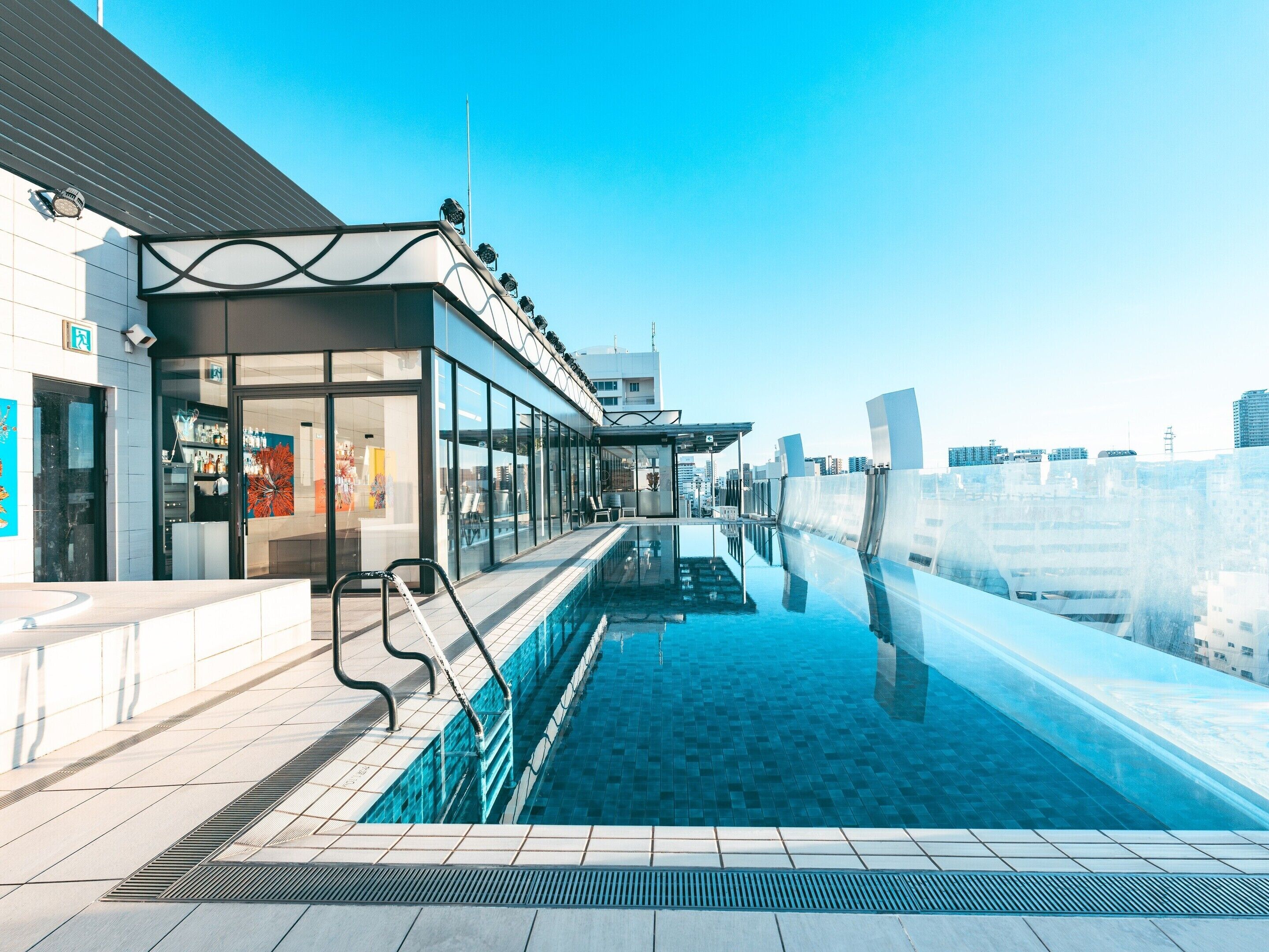 A rooftop pool with clear blue water, a glass barrier, and a view of the city skyline.