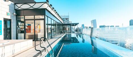 A rooftop pool with clear blue water, a glass barrier, and a view of the city skyline.