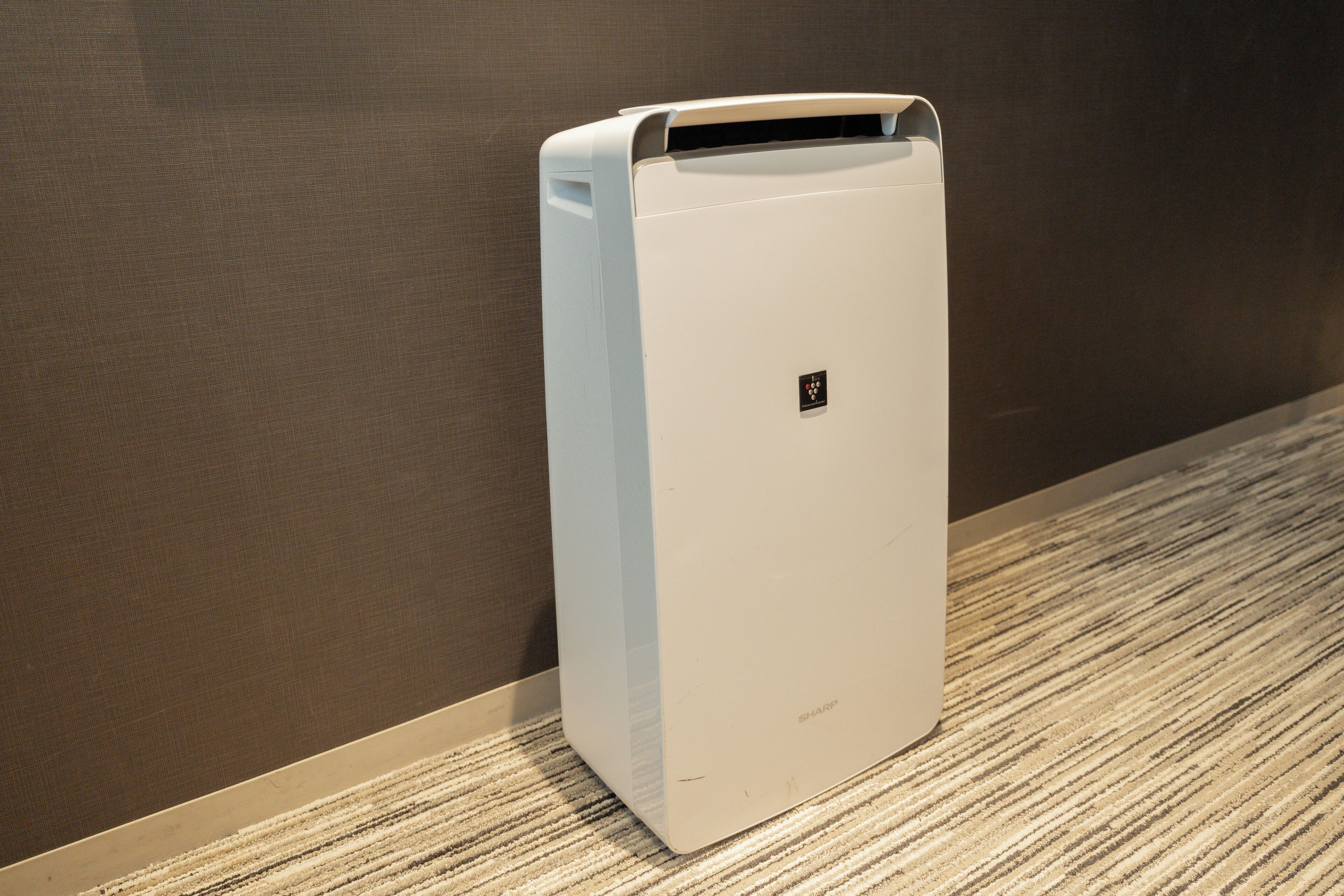 A white air conditioning unit against a brown wall with a textured carpet.