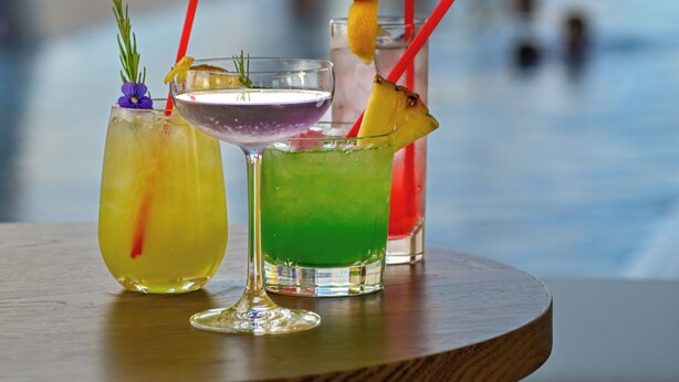 Drei Cocktails auf einem Holztisch, im Hintergrund eine unscharfe Stadtansicht.