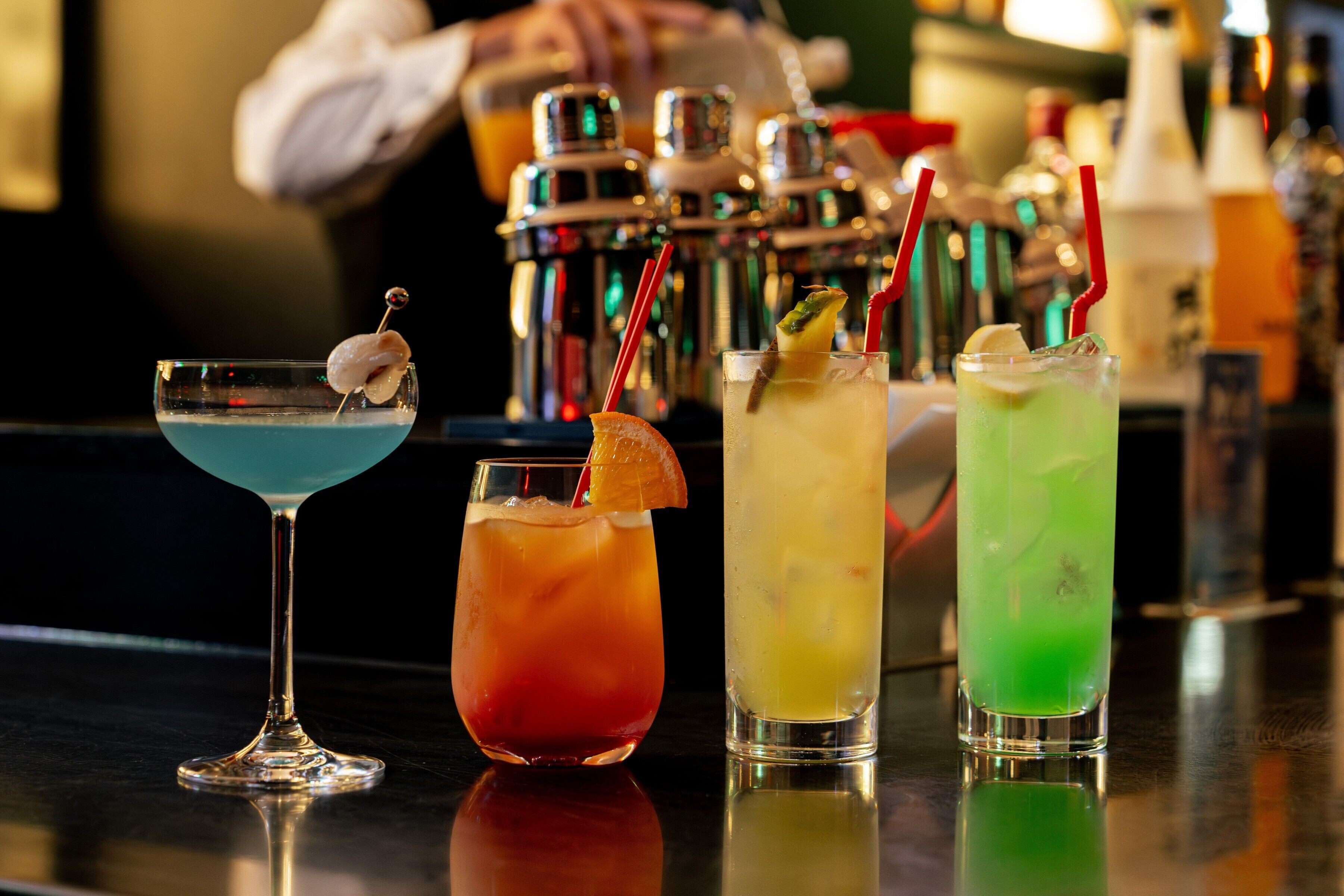A bar with three different cocktails, each with a garnish and a straw.