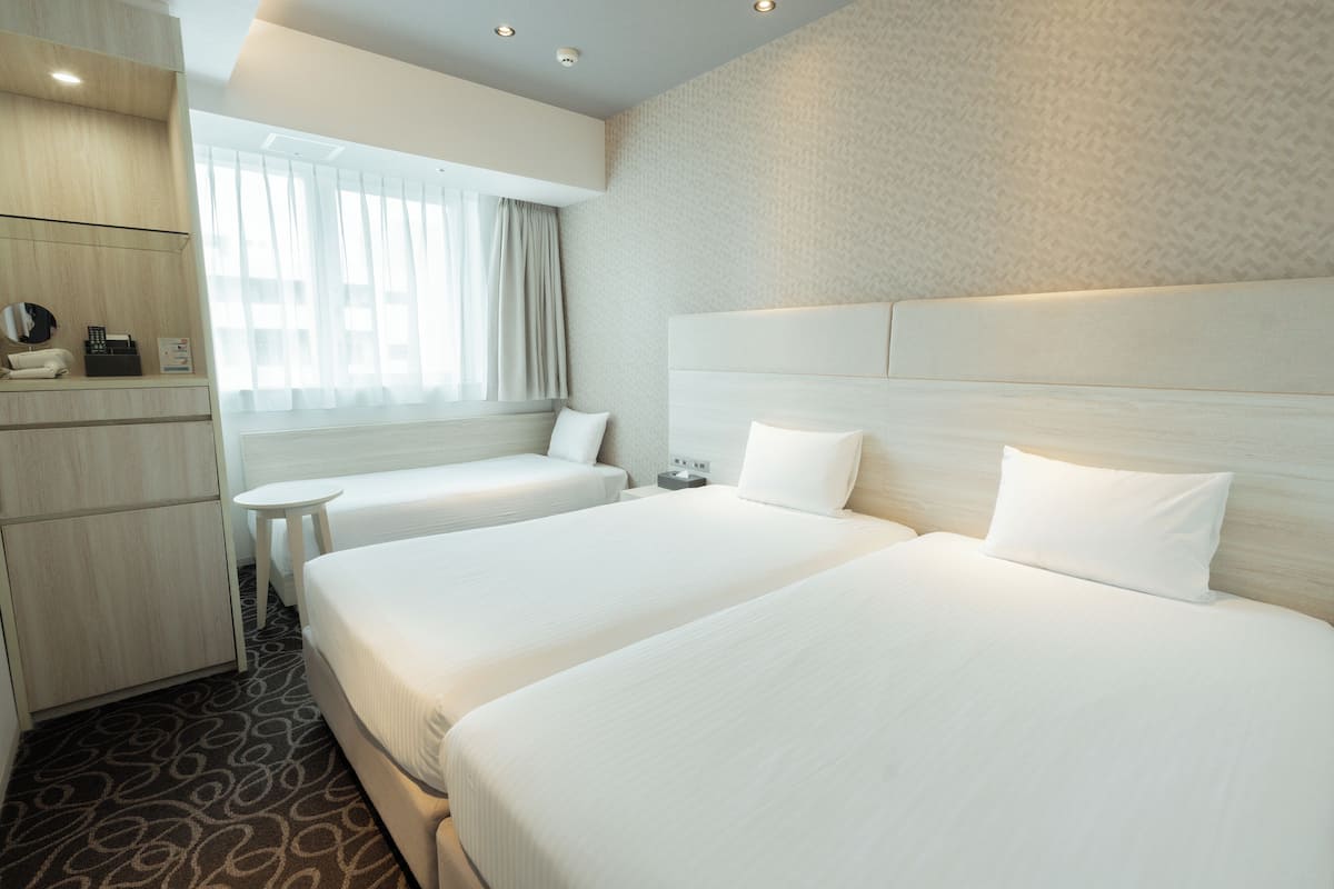 Habitació d'hotel amb dos llits, una taula petita, un escriptori i una finestra amb cortines.