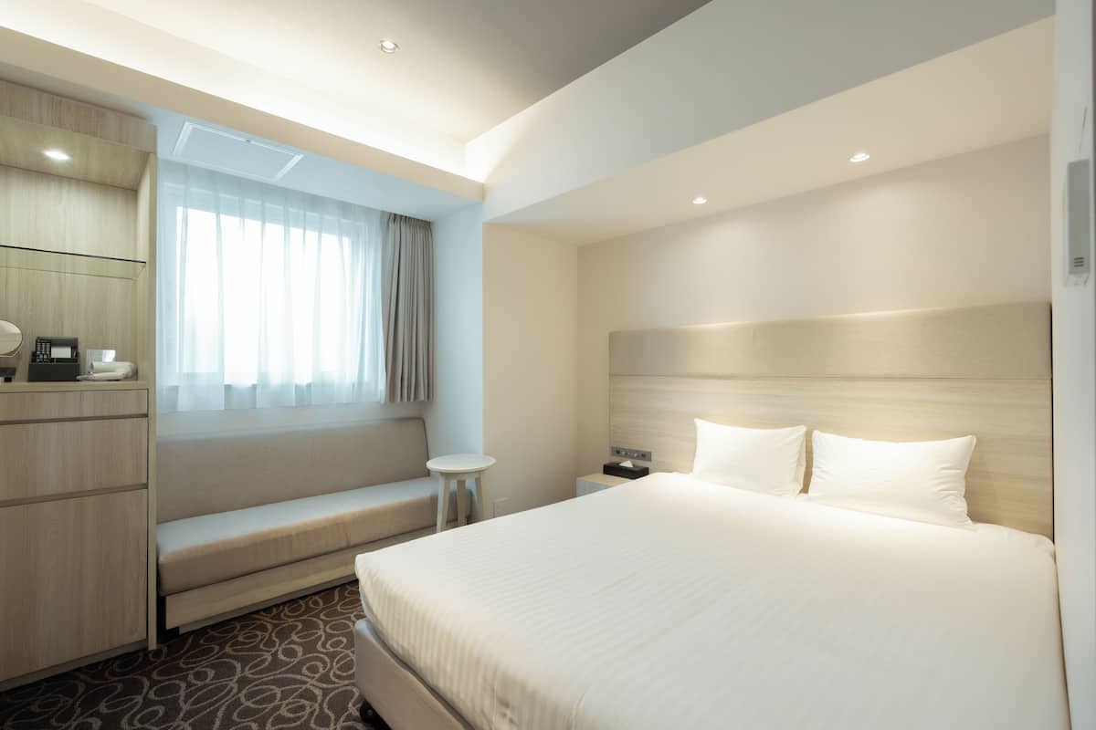 Una habitació d'hotel moderna amb un llit gran, zona de seients, escriptori amb telèfon i finestra amb cortines.