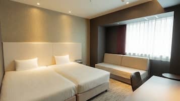 Een hotelkamer met twee bedden, een bank, een tafeltje en een raam met gordijnen.
