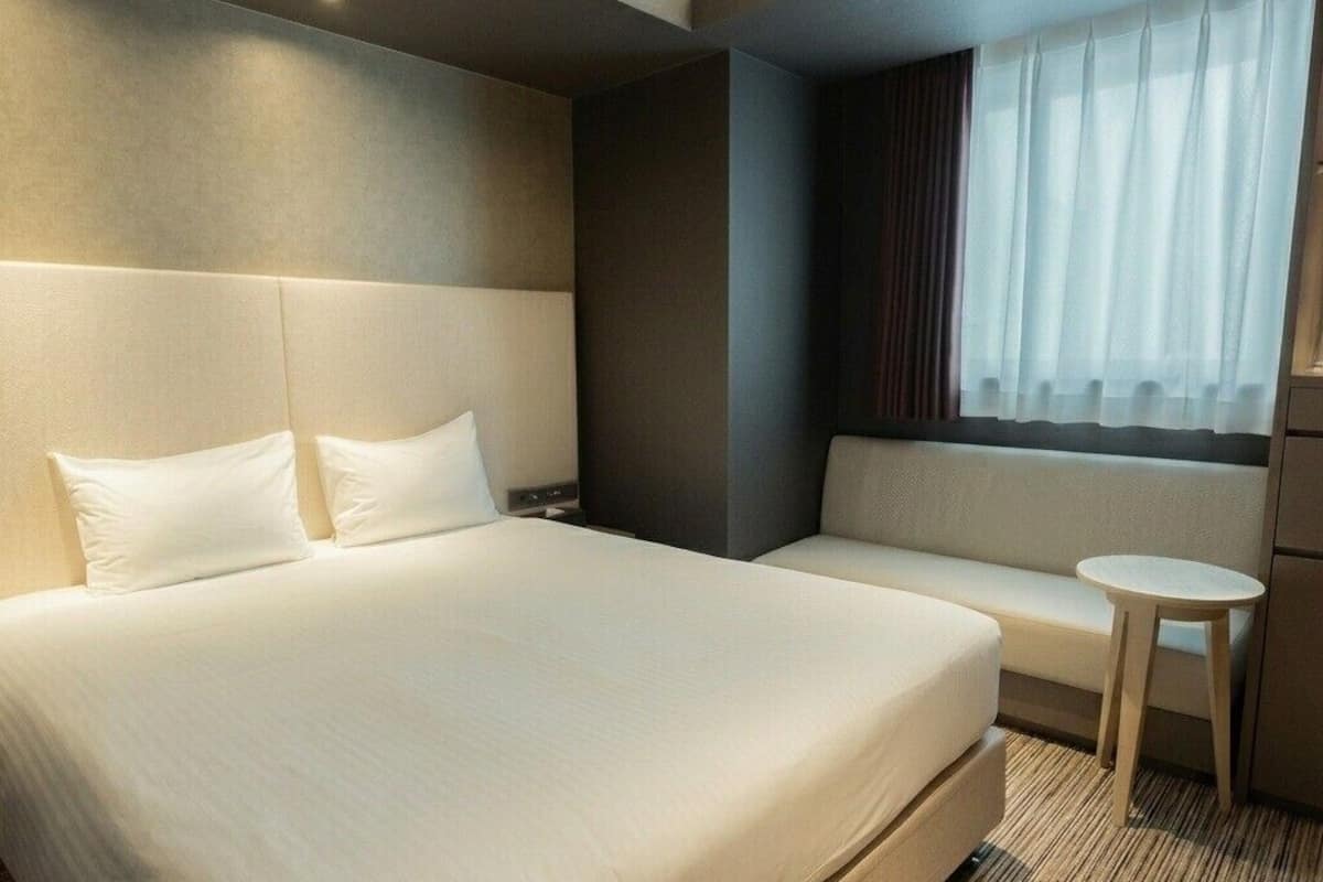 Habitació d'hotel amb un llit gran, un sofà, una taula petita i una finestra amb cortines.