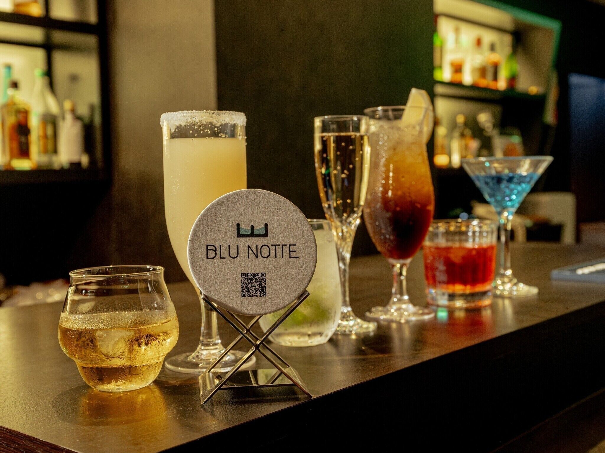 A bar area with a variety of drinks and a sign reading "BLU NOTTE" with a QR code.