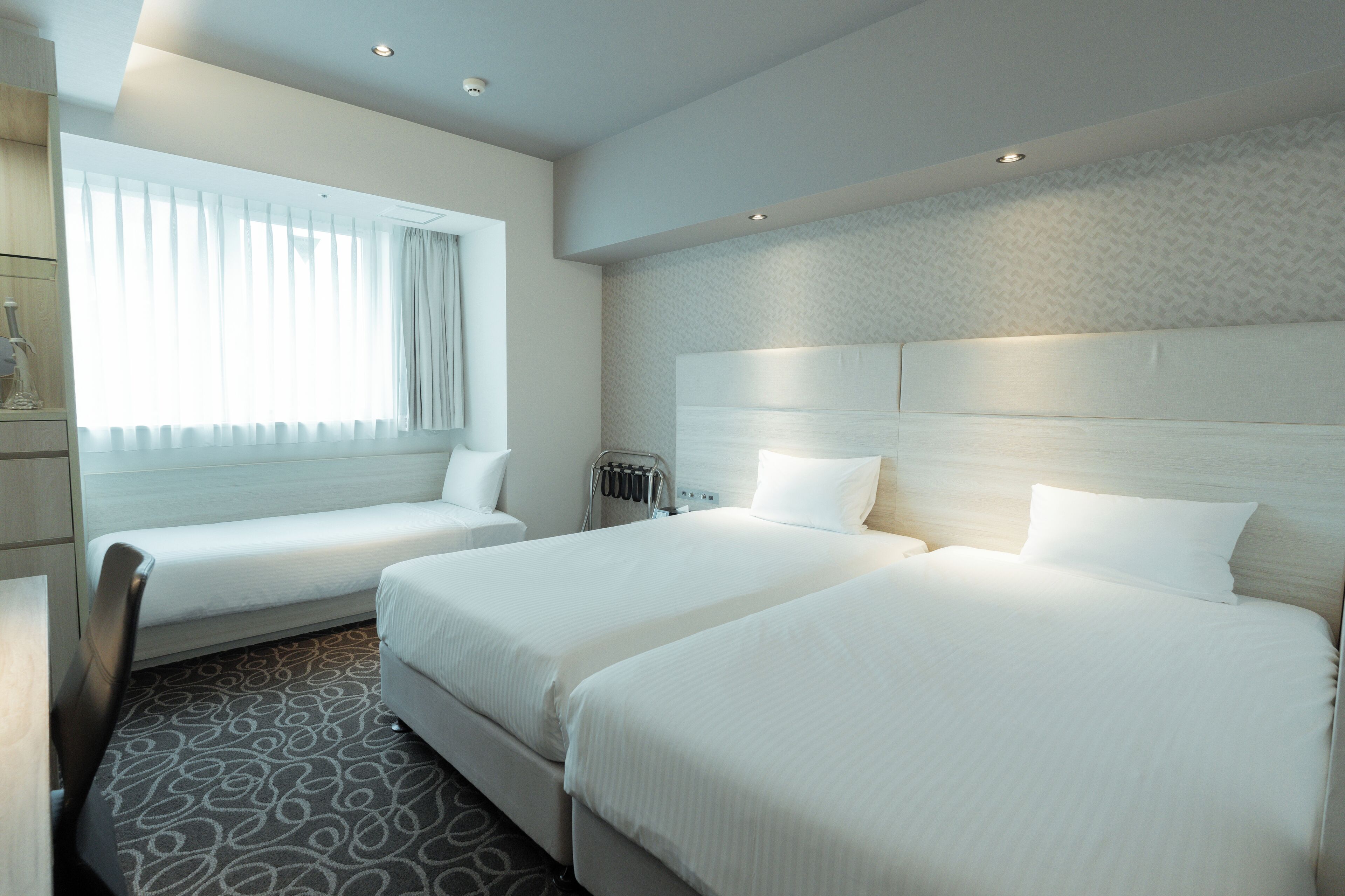 A hotel room with two beds, a desk, a chair, a radiator, and a window with curtains.