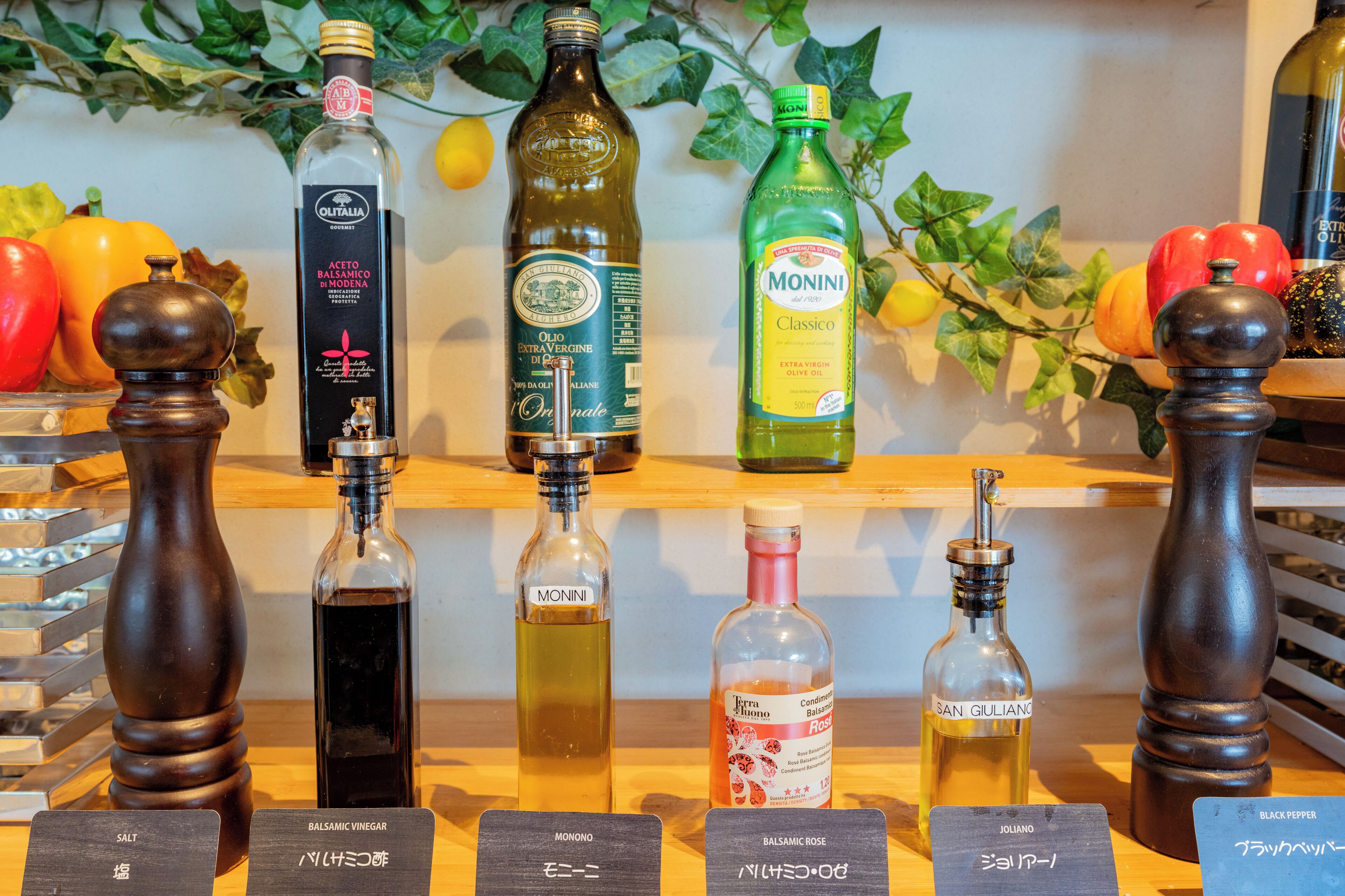 A selection of olive oil bottles with labels in various languages, accompanied by wooden salt and pepper shakers.