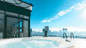 Un jacuzzi en la azotea con vistas a la ciudad, puerta de entrada de vidrio y un área de descanso con sillas.