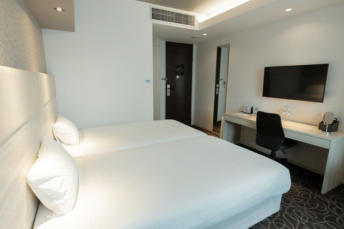 Habitación de hotel con una cama grande, un escritorio, una silla, un televisor de pantalla plana y una puerta que da a un baño.