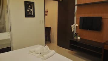 A hotel room with a bed, a TV mounted on the wall, a door leading to another room, and a small table with a vase of flowers.