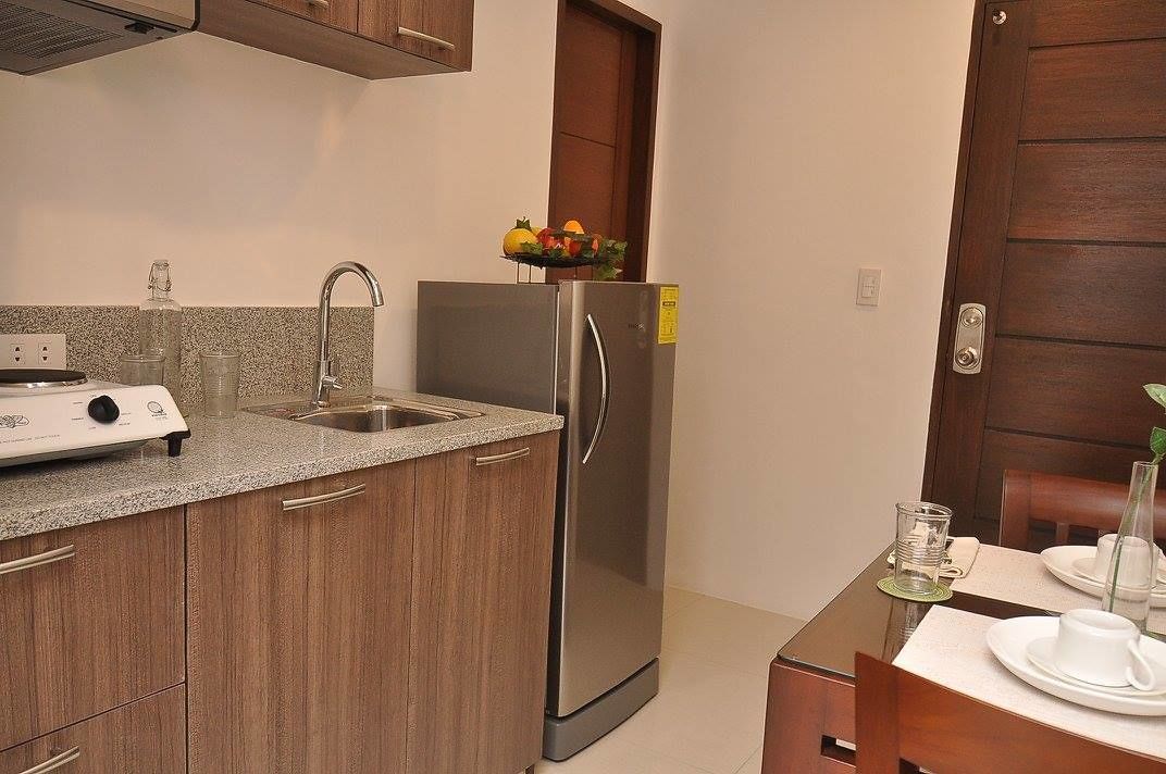 A compact kitchen with a stainless steel refrigerator, a built-in stove, and a sink. There is a dining table with white tableware.