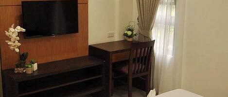 Habitación de hotel con cama, televisor montado en un panel de madera, escritorio con silla y ventana con cortinas.