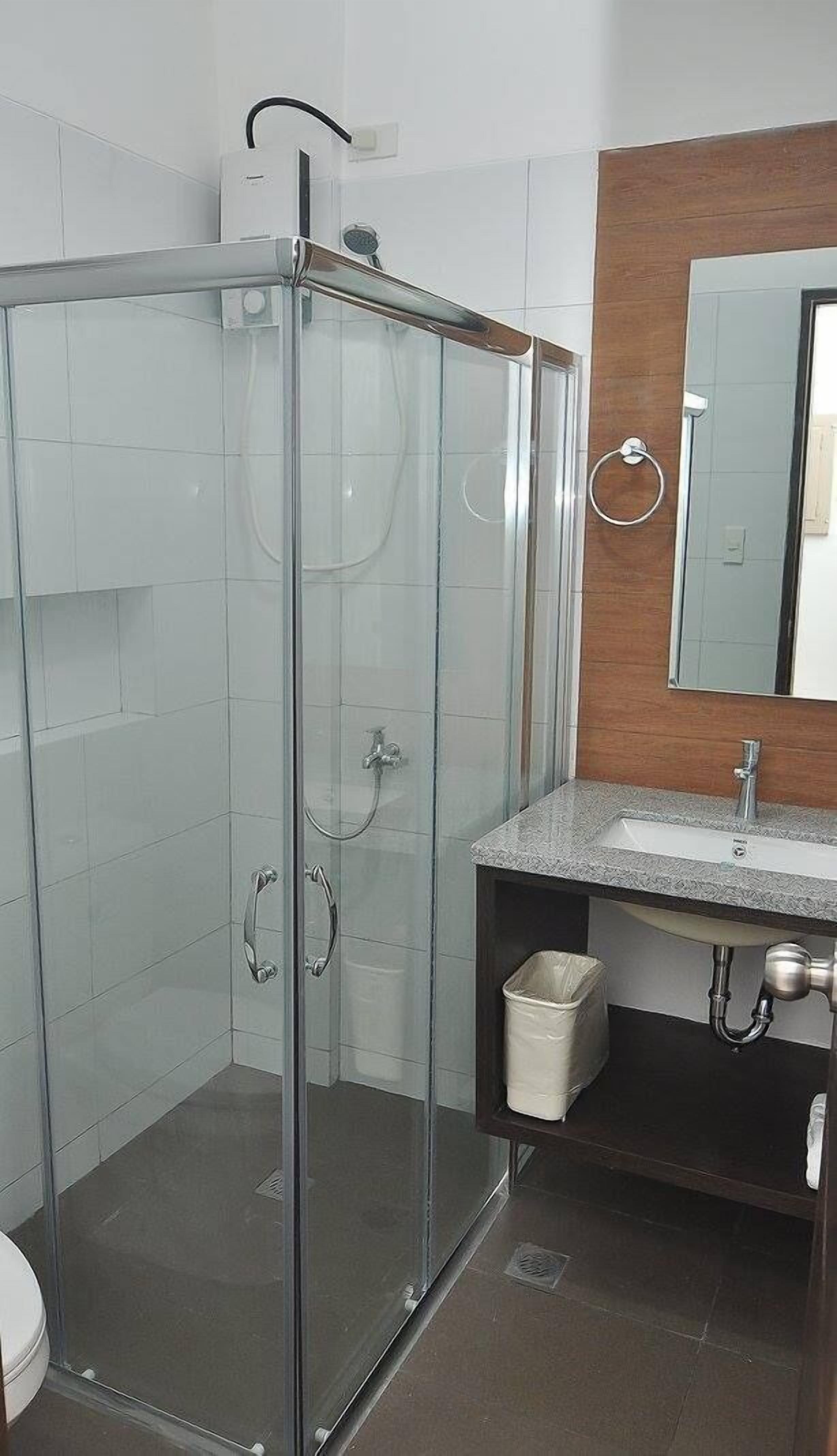 Ein Badezimmer mit Duschkabine, Waschbecken mit Spiegel und Mülleimer.