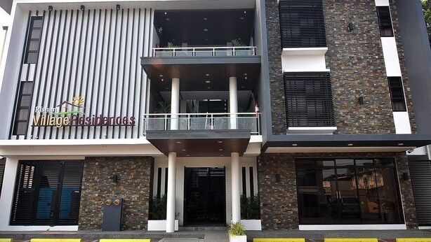 A modern building with a sign for 'Rishawn Village Residences'. It features a balcony, a stone facade, and a flat roof. - Rishan Village Residences (Angeles City)