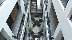 A modern building with a central courtyard featuring a seating area with tables and chairs, surrounded by potted plants. - Rishan Village Residences (Angeles City)